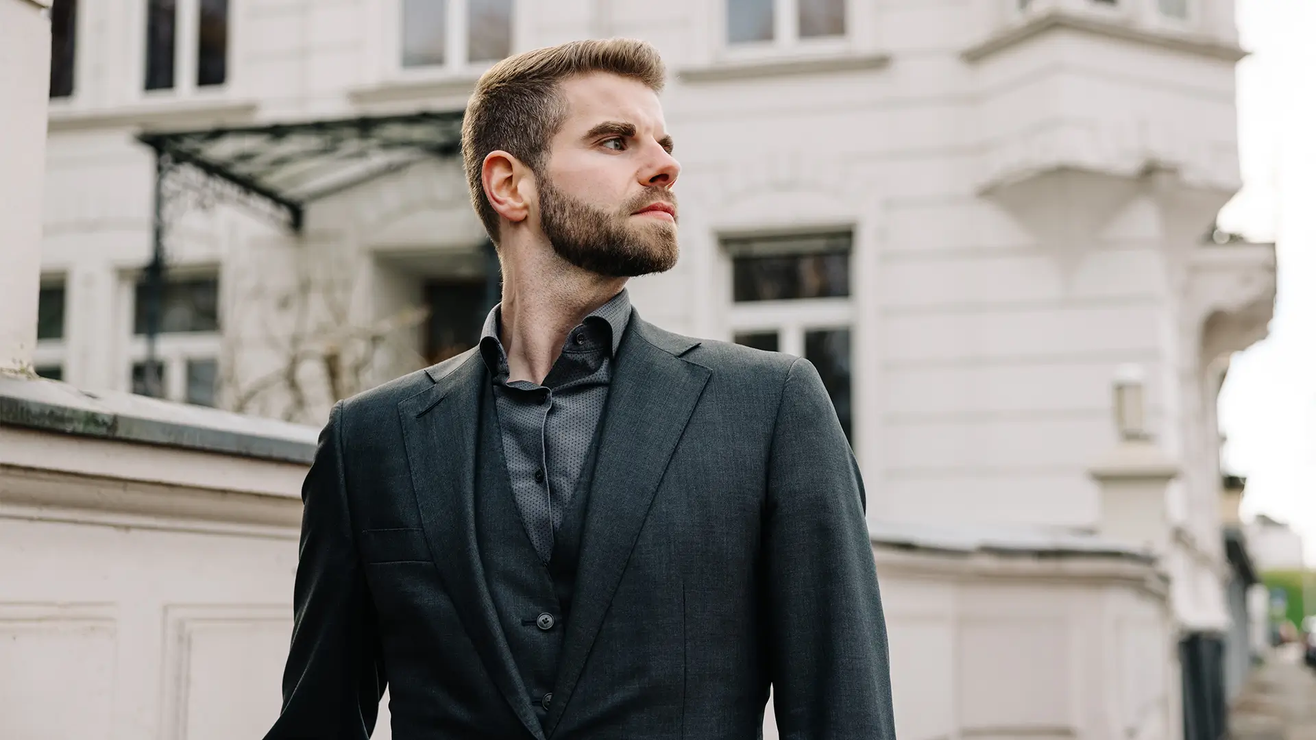 Julian Schwarz im Anzug blickt zur Seite, im Hintergrund die Fassade eines historischen Gebäudes.