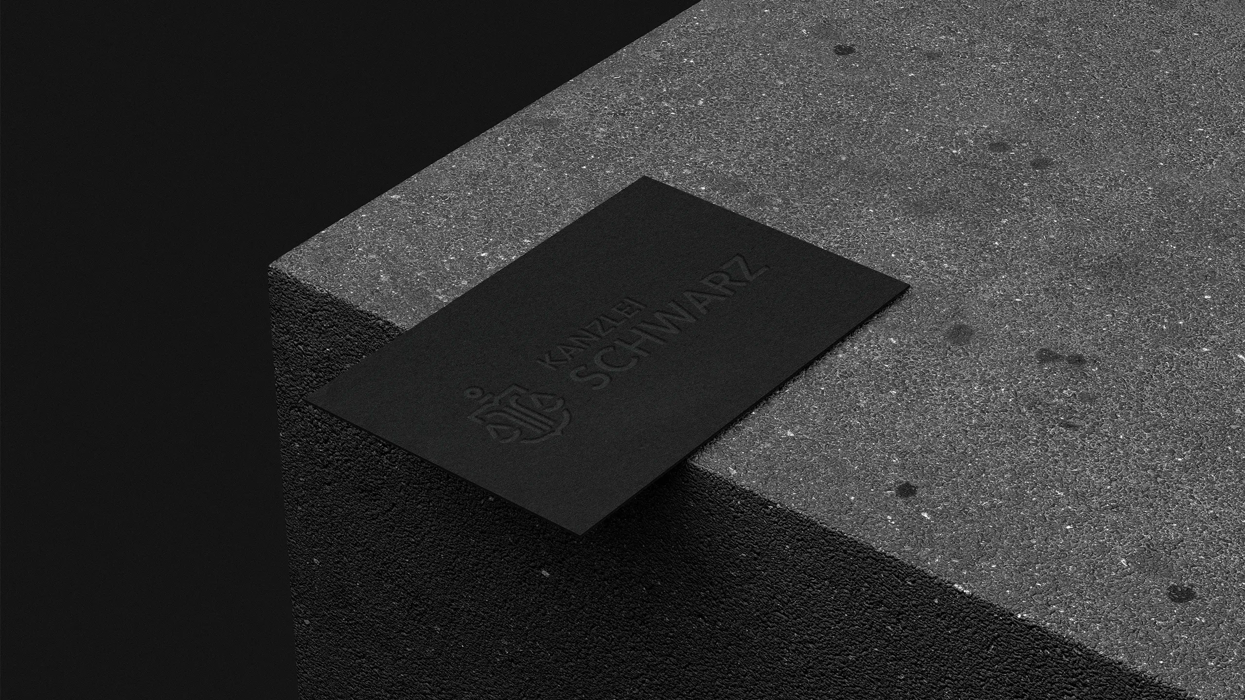 Schwarze, minimalistische Visitenkarte der Kanzlei Schwarz mit geprägtem Logo und Schriftzug, platziert auf einer dunklen Betonstufe – Darstellung eines hochwertigen und reduzierten Markenauftritts.