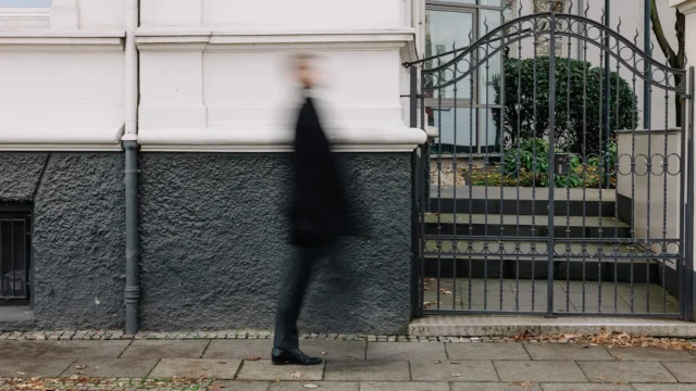 Person in dunkler Kleidung geht an der Fassade eines historischen Gebäudes vorbei.