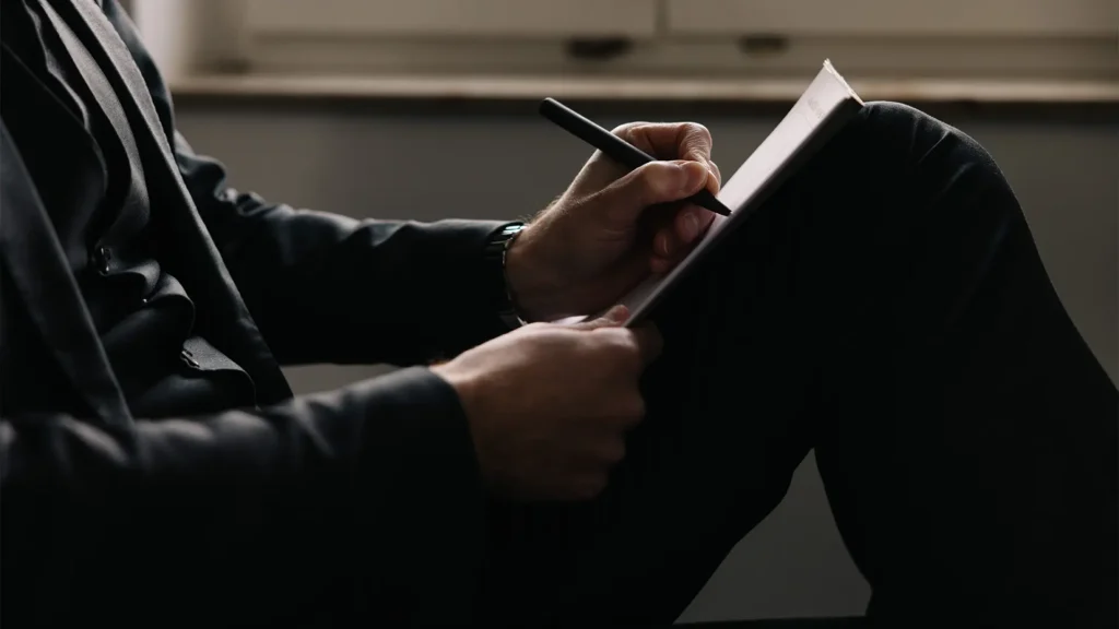Person im Anzug macht handschriftliche Notizen in einem Notizbuch.