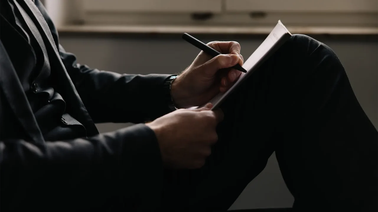 Person im Anzug macht handschriftliche Notizen in einem Notizbuch.